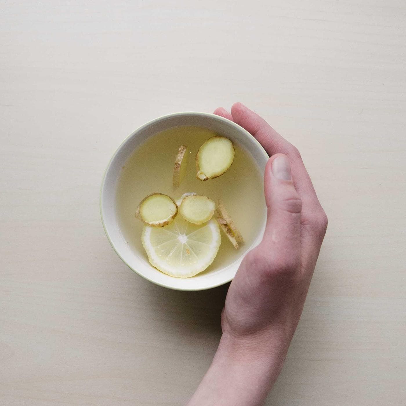 A hand holding a white bowl on a clean pale countertop