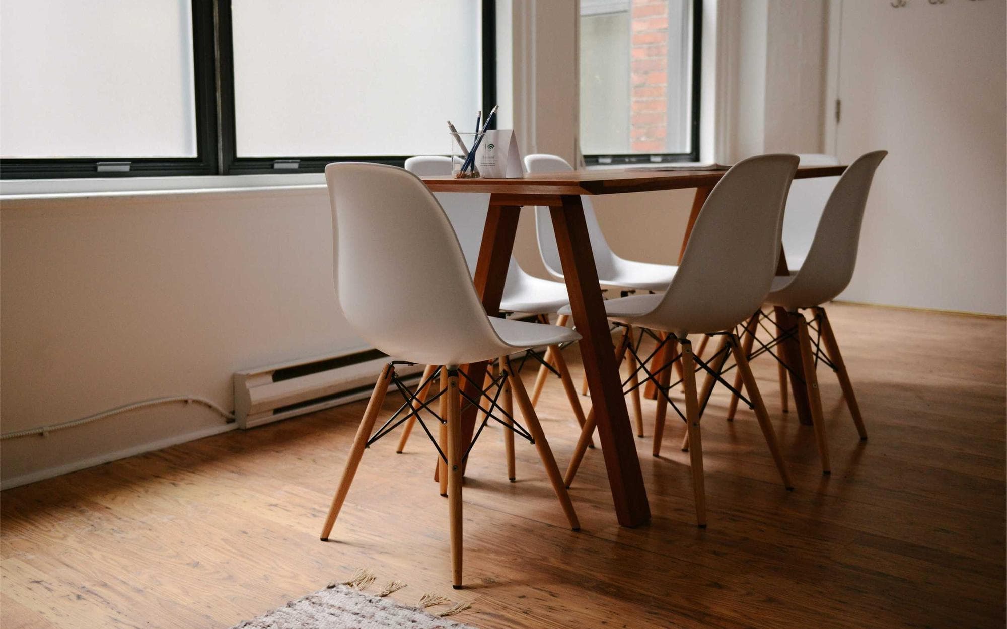 A bright, tidy dining room with white chairs and sunlight from large windows